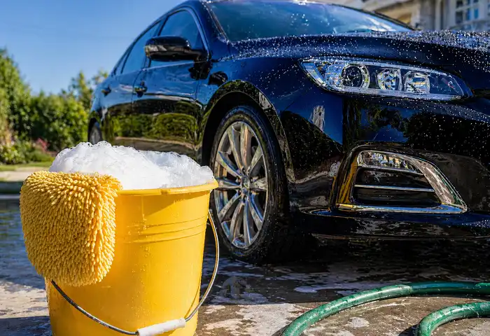 Home made car shampoo bucket with foam beside clean black car