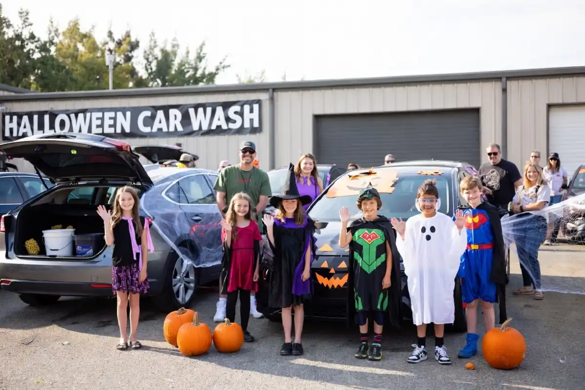 Families and children at a Halloween haunted car wash community event with pumpkins and costumes