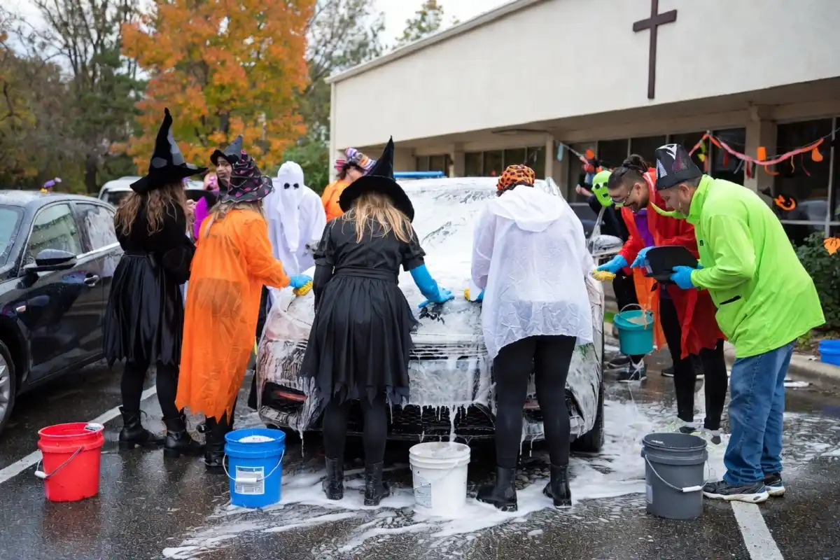 Volunteers in Halloween costumes hosting a haunted car wash fundraiser at a school parking lot