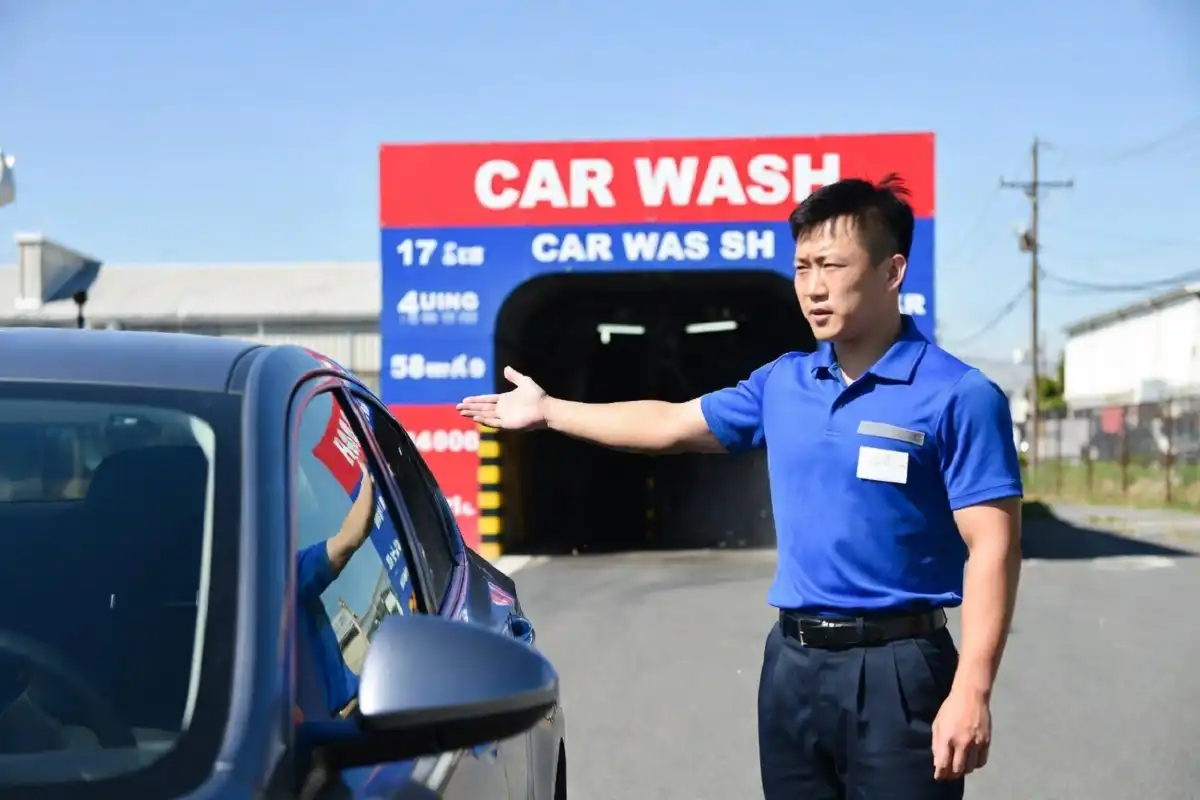 A car wash attendant in uniform guiding a car into an automatic wash tunnel