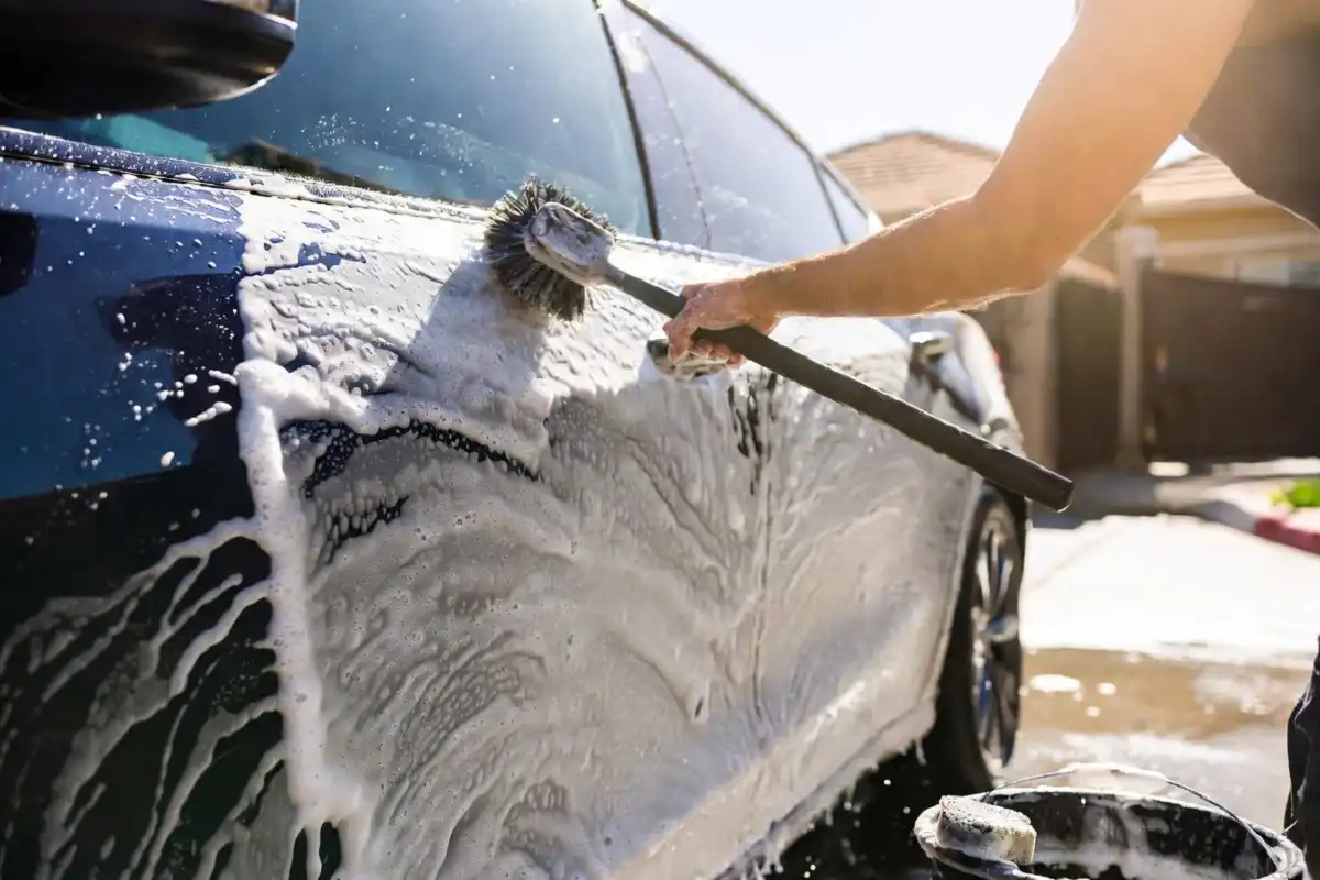 Person using a car wash brush to clean a vehicle with soapy water