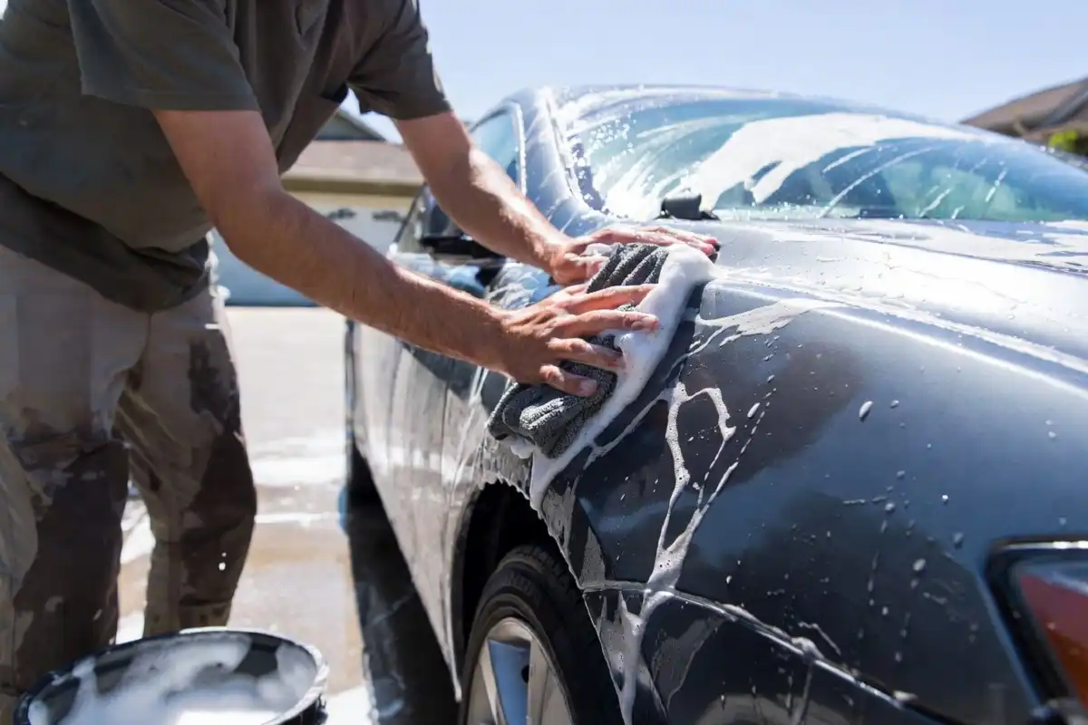 A person washing a car using a microfiber mitt and soapy water from a bucket