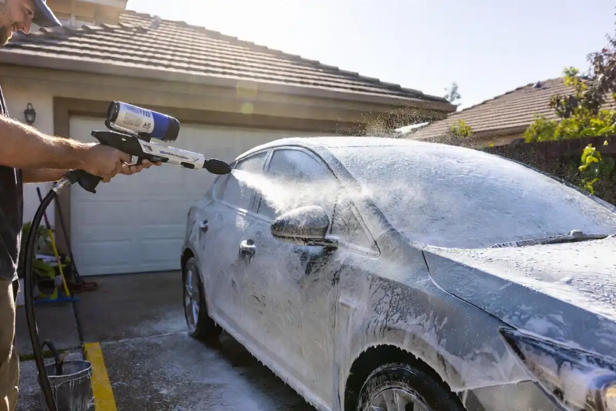 Person washing car at home with foam cannon as DIY alternative to splash car wash