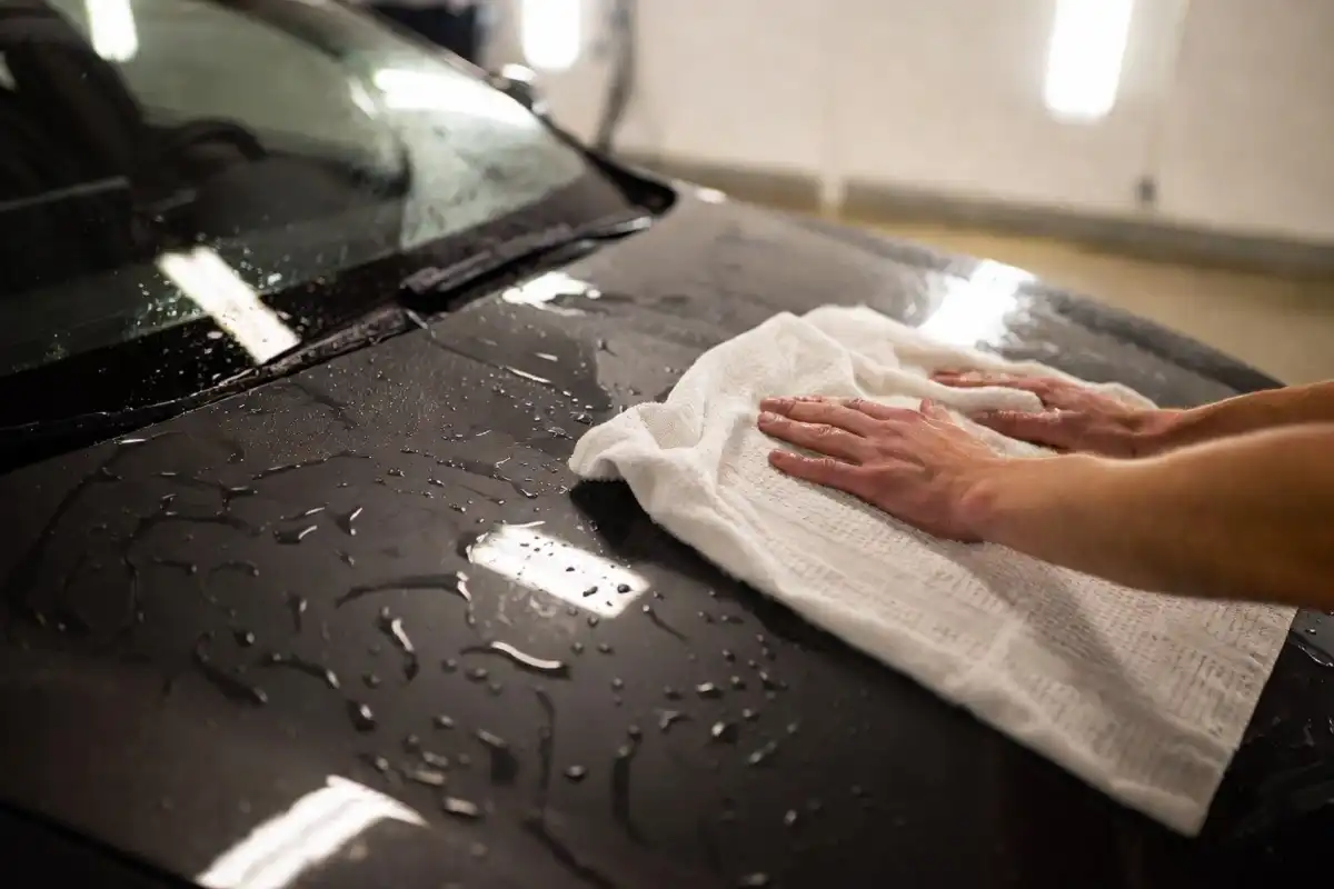 Person drying a freshly washed black car with a clean microfiber towel