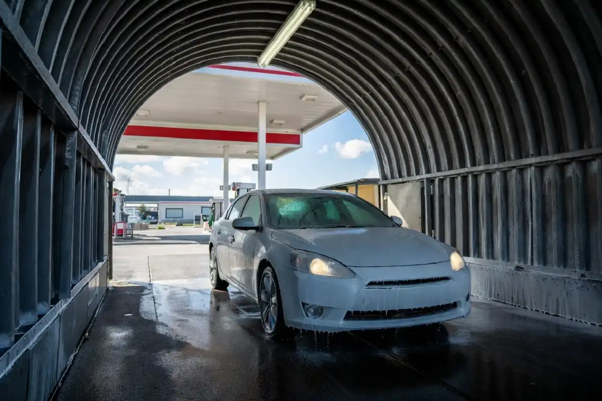 A clean car exiting a gas station car wash tunnel after a full wash cycle