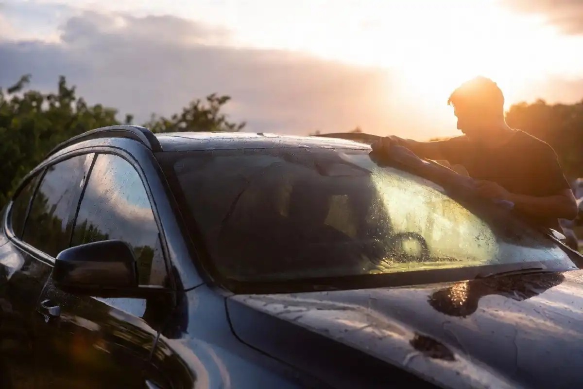Person drying a black car with a large microfiber towel after a hand car wash