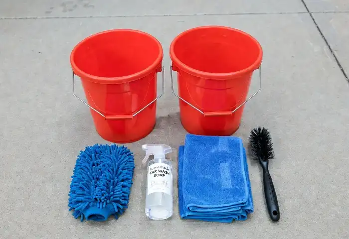 DIY car wash supplies including two buckets, microfiber mitt, and car soap on driveway