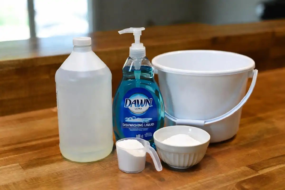 Homemade car wash soap vinegar ingredients including white vinegar, dish soap, and baking soda on wooden surface