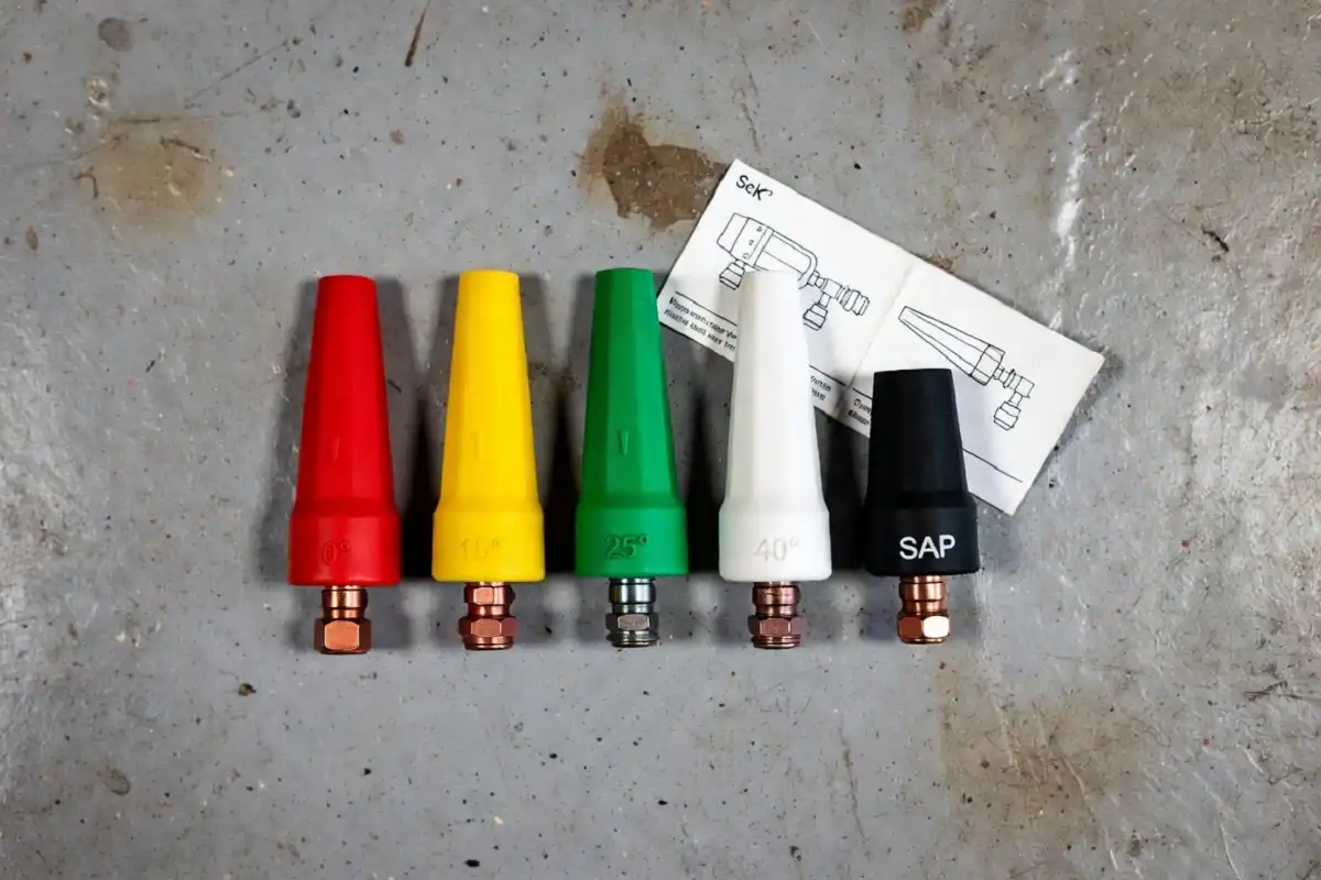 Five color-coded pressure washer nozzle tips laid out on a garage floor for home car wash machine use