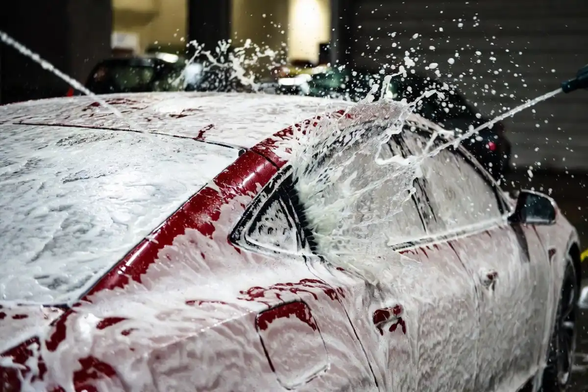 Water jets rinsing foam off a red car during a touch free wash cycle