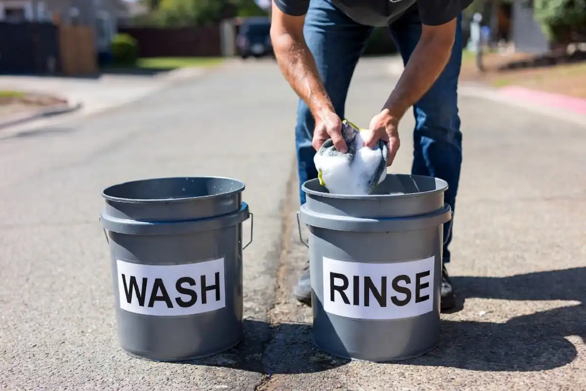 Two bucket hand car wash method with wash and rinse buckets on a driveway