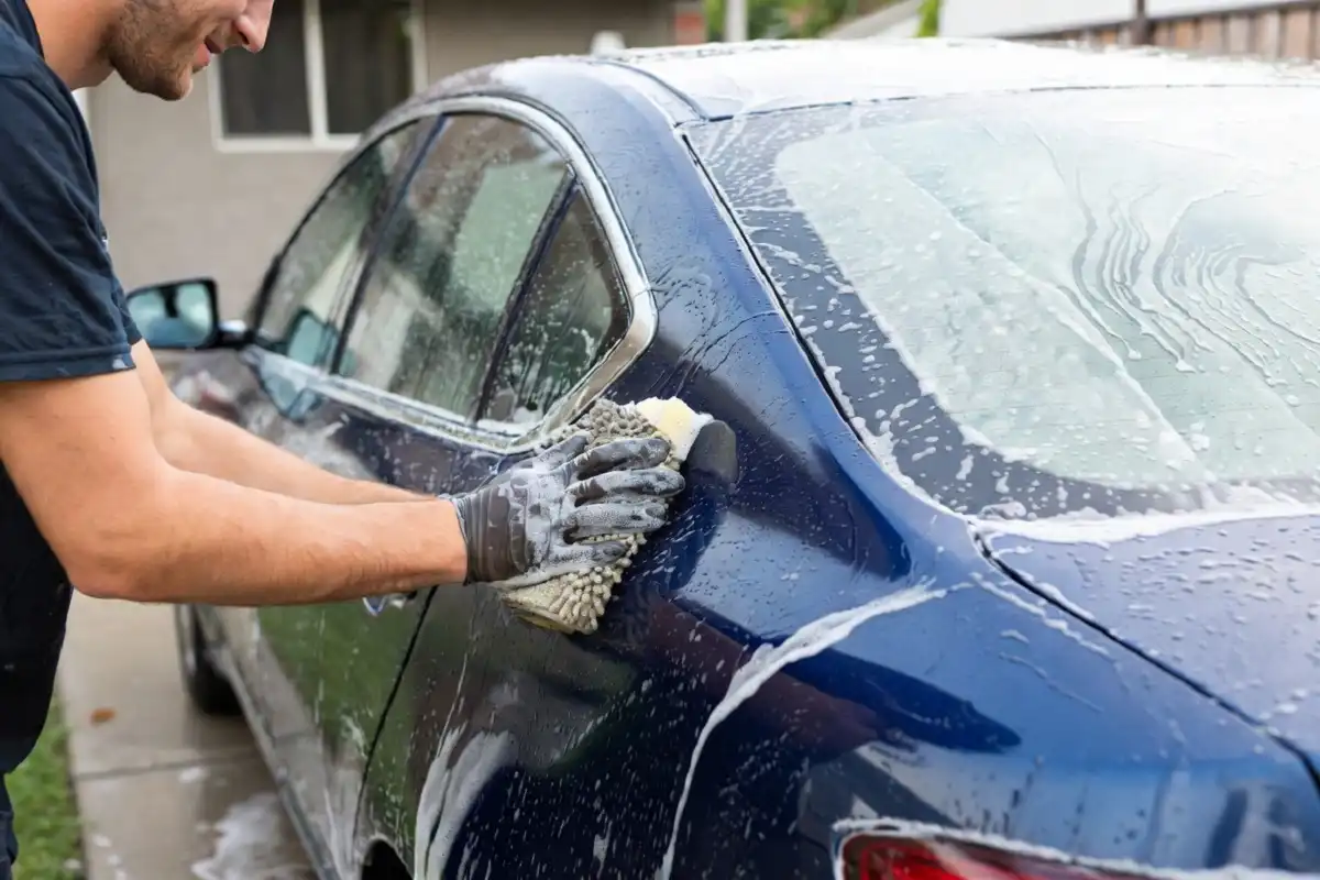 Person using a microfiber wash mitt to clean a car door panel at home