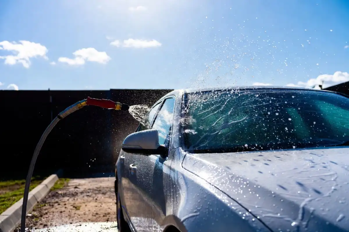 A white car being rinsed during a white water car wash on a sunny day
